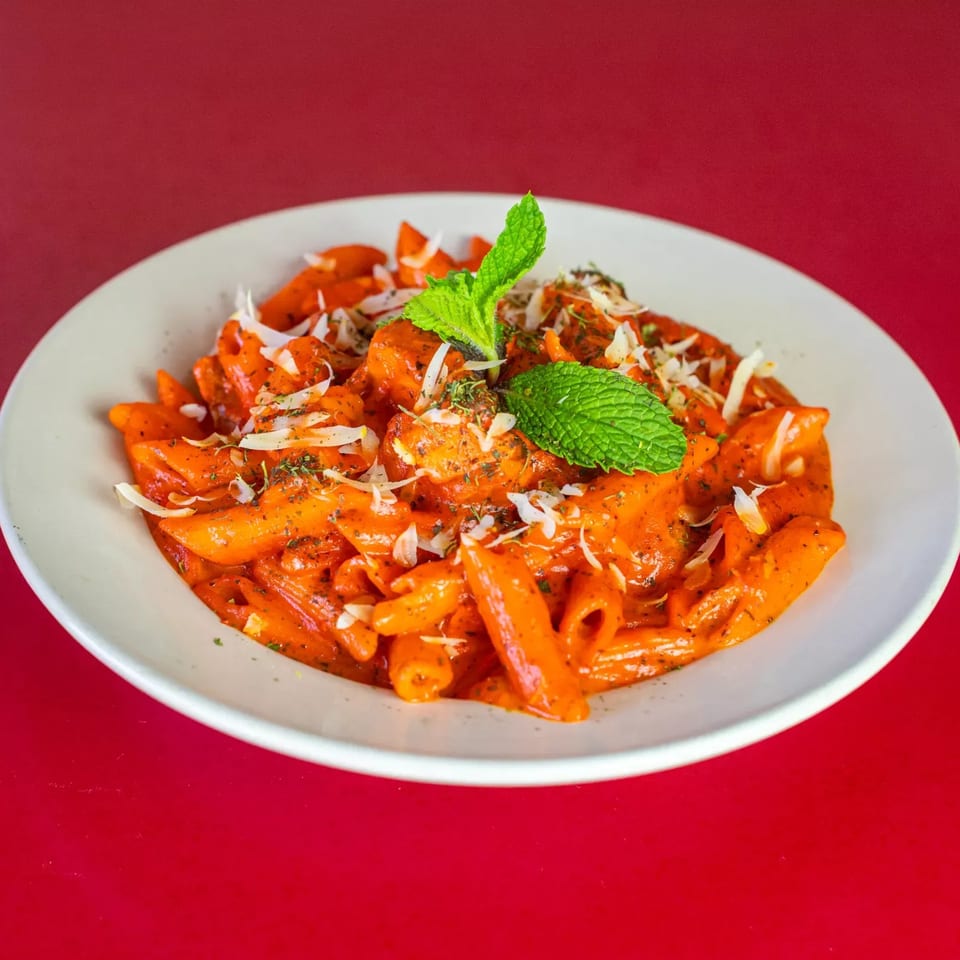Penne pasta in a creamy orange sauce, topped with shredded cheese and fresh mint leaves.