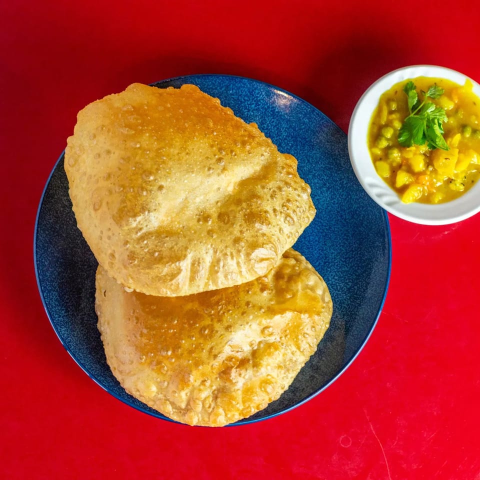 Two golden-brown Indian puri breads on a blue plate, with a side of potato and pea curry.