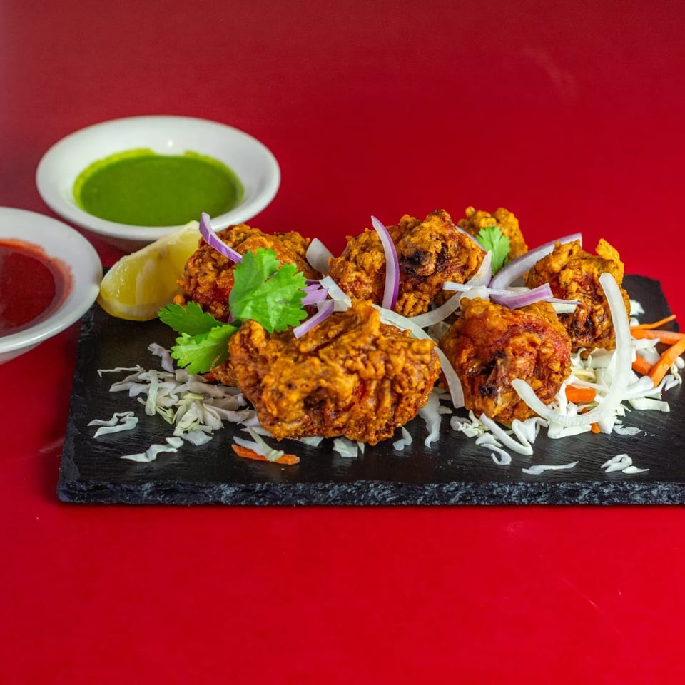 Indian chicken pakora, garnished with cilantro, red onion, and lemon, served with two dipping sauces.