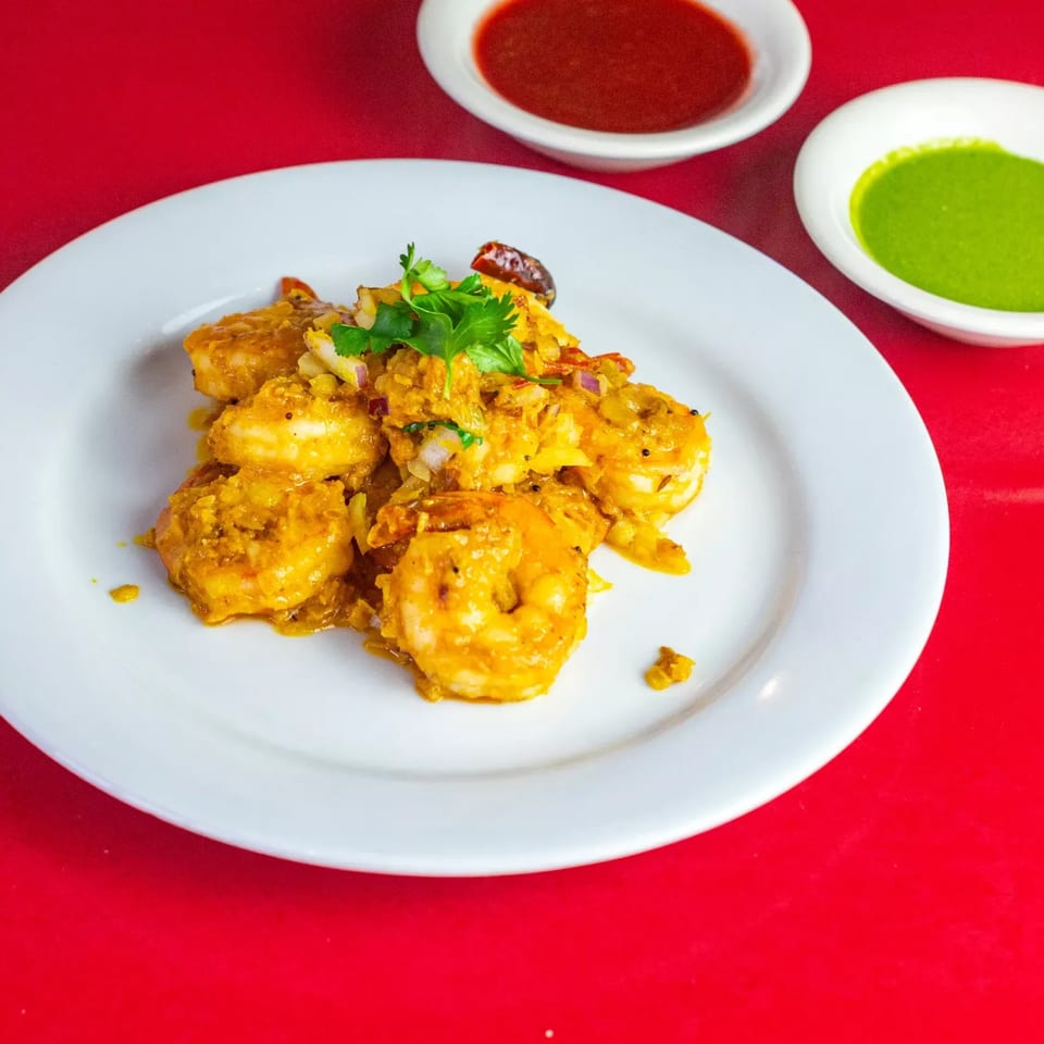 Indian shrimp curry with cilantro, red onions, and two dipping sauces on a red background.